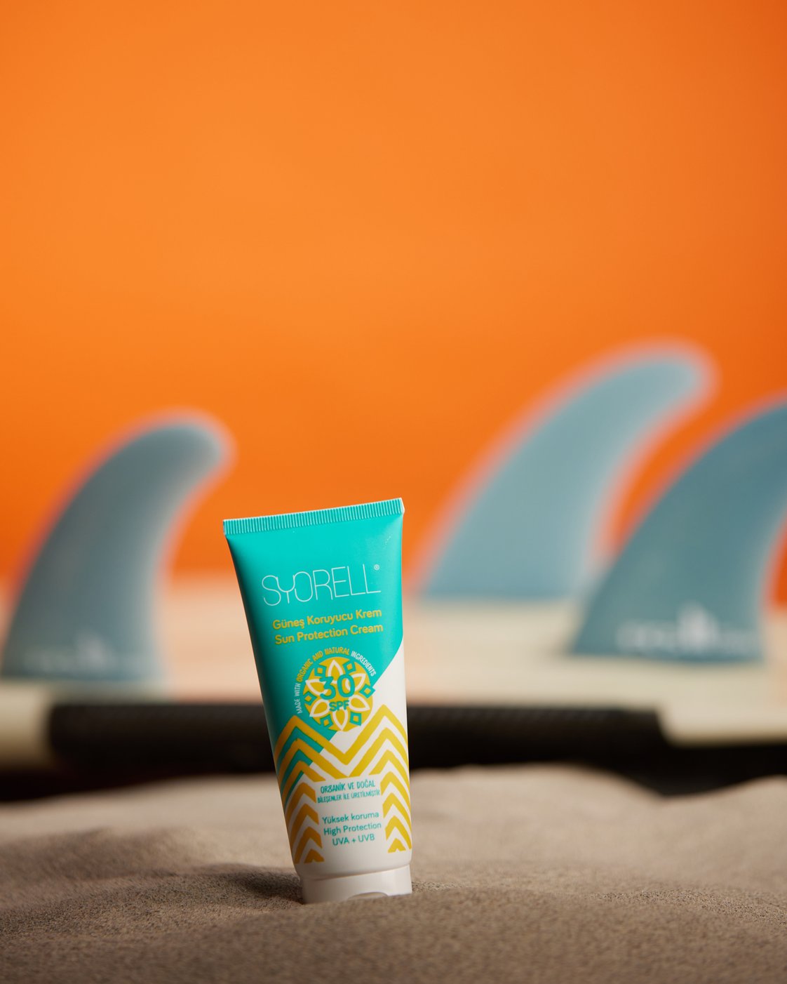 Syorell Sunscreen for Dry and Damaged Skin SPF 30 turquoise tube on sand with surfboard fins on orange background